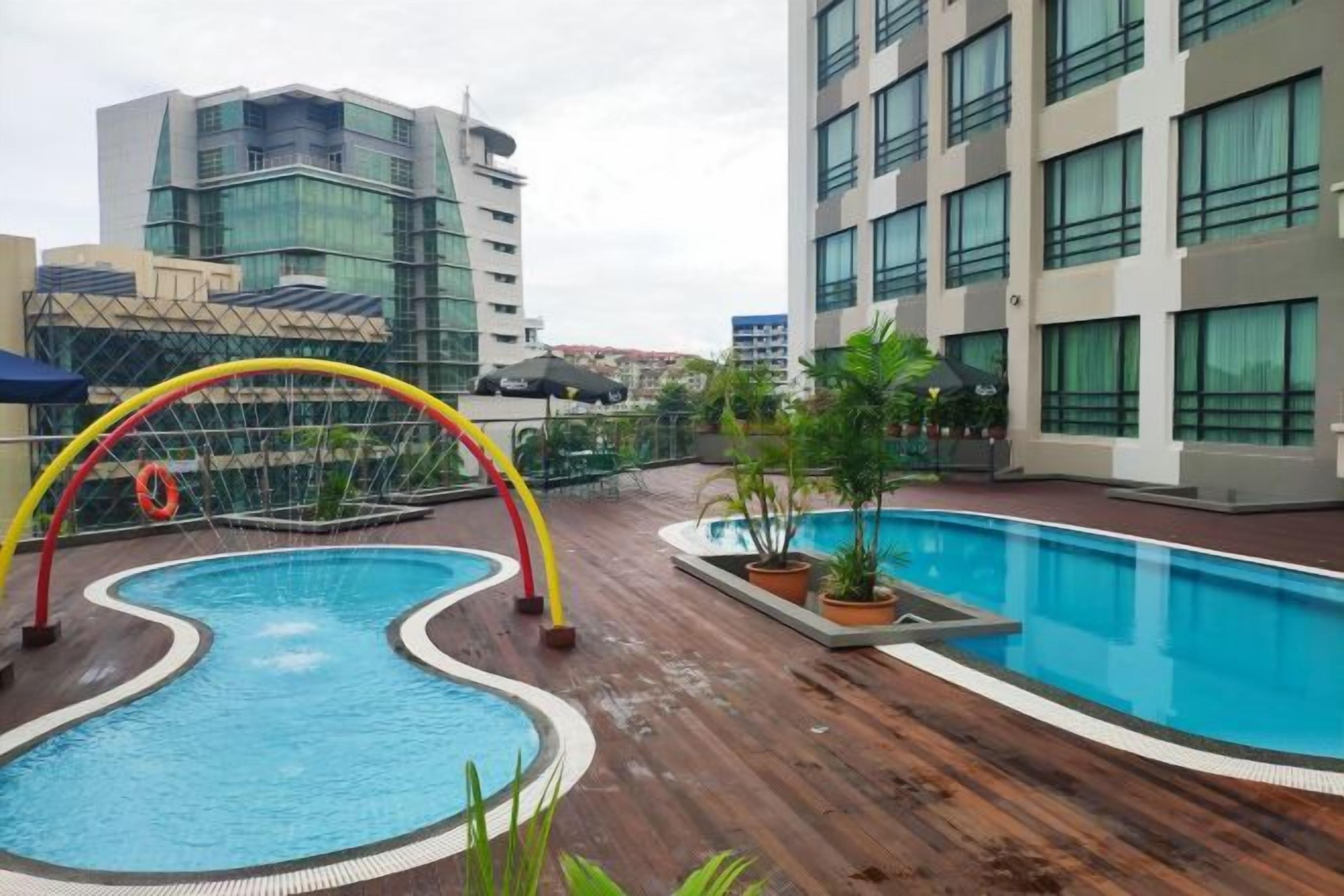 A rooftop pool with a unique arch structure, surrounded by potted plants and a wooden deck.