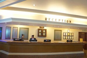 A reception desk with a 'RECEPTION' sign above, a receptionist, and a clock on the wall. - Sabah Oriental Hotel Kota Kinabalu (Kota Kinabalu)
