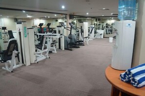 Un gimnasio con diversas máquinas de ejercicio, un dispensador de agua y un perchero para toallas.