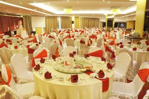 Une salle de banquet avec des tables rondes dressées pour un événement formel, agrémentée de nappes blanches et de rubans rouges.
