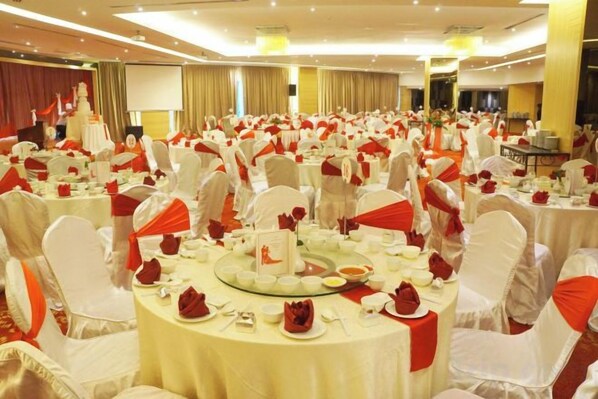 Un salón de banquetes con mesas redondas dispuestas para un evento formal, con manteles blancos y fajas rojas.