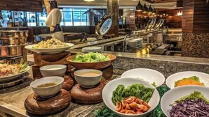 A buffet area with various dishes and bowls of food, a chef statue, and a modern kitchen in the background. - Sabah Oriental Hotel Kota Kinabalu (Kota Kinabalu)