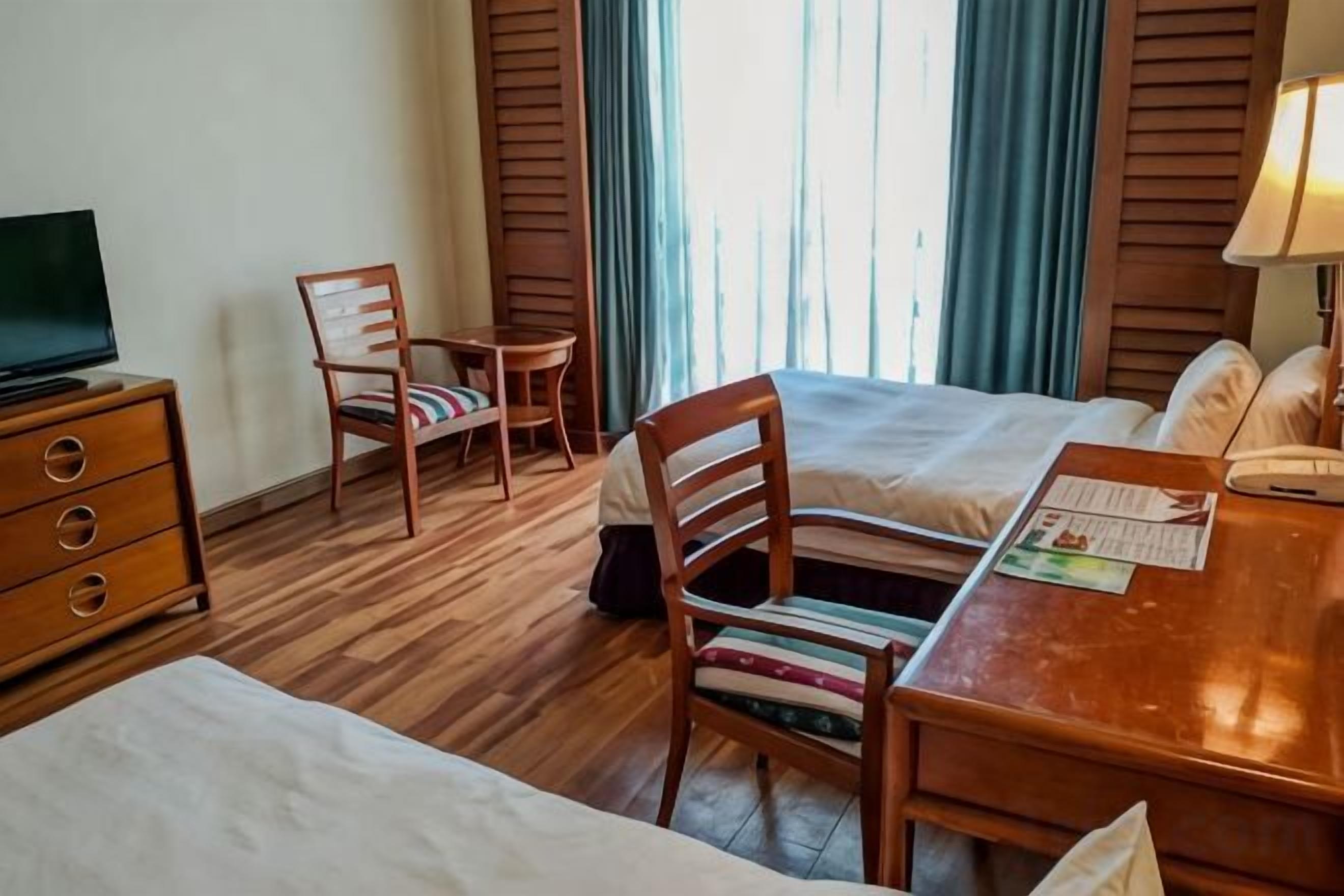 A hotel room with a bed, a desk, a chair, a television, and a window with curtains.