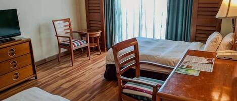 A hotel room with a bed, a desk, a chair, a television, and a window with curtains.