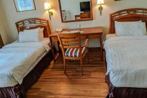 A hotel room with two beds, a desk, a chair, and a mirror.