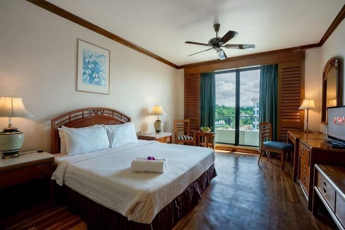 A hotel room with a bed, a desk, a chair, a television, and a balcony with a view.