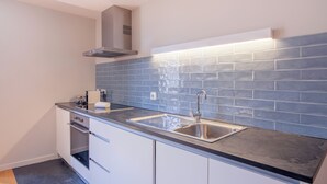A modern kitchen with a double sink, stainless steel appliances, and a blue-tiled backsplash. - ALMADA 151 (Porto)