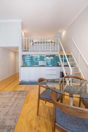 A modern kitchen with white cabinets, a blue backsplash, and a wooden staircase. - ALMADA 151 (Porto)