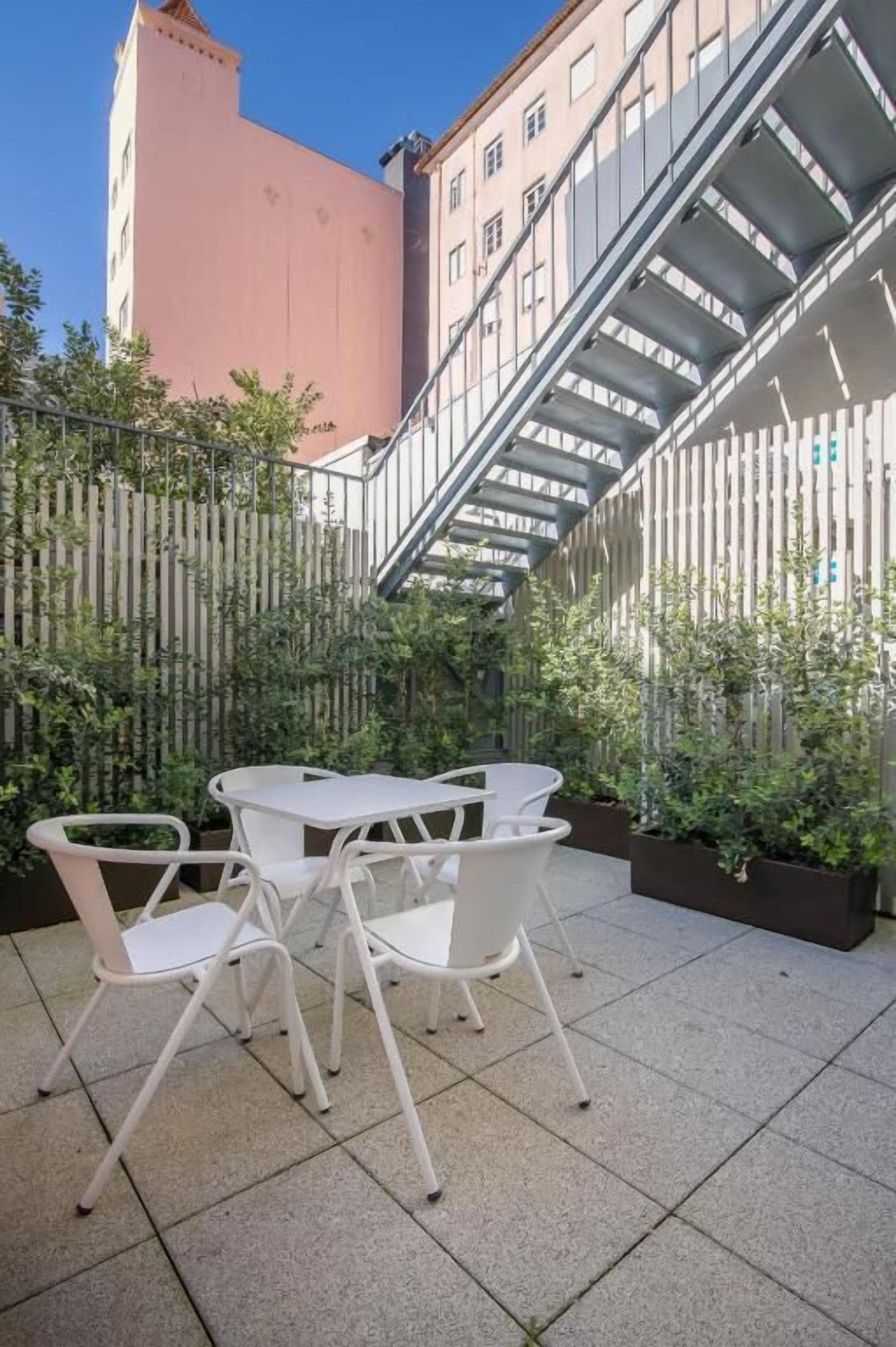 A courtyard with a table and chairs, surrounded by a wooden fence and potted plants.