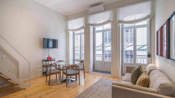 A spacious living area with a wooden floor, a dining table with chairs, a sofa, and a TV mounted on the wall. - ALMADA 151 (Porto)