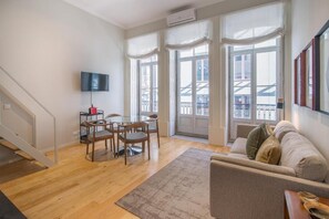 A spacious living area with a wooden floor, a dining table with chairs, a sofa, and a TV mounted on the wall. - ALMADA 151 (Porto)