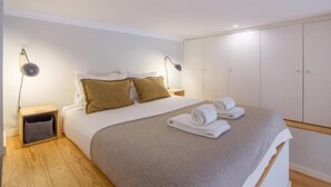 A bedroom with a bed, two bedside lamps, a nightstand, a wardrobe, and a small basket. - ALMADA 151 (Porto)