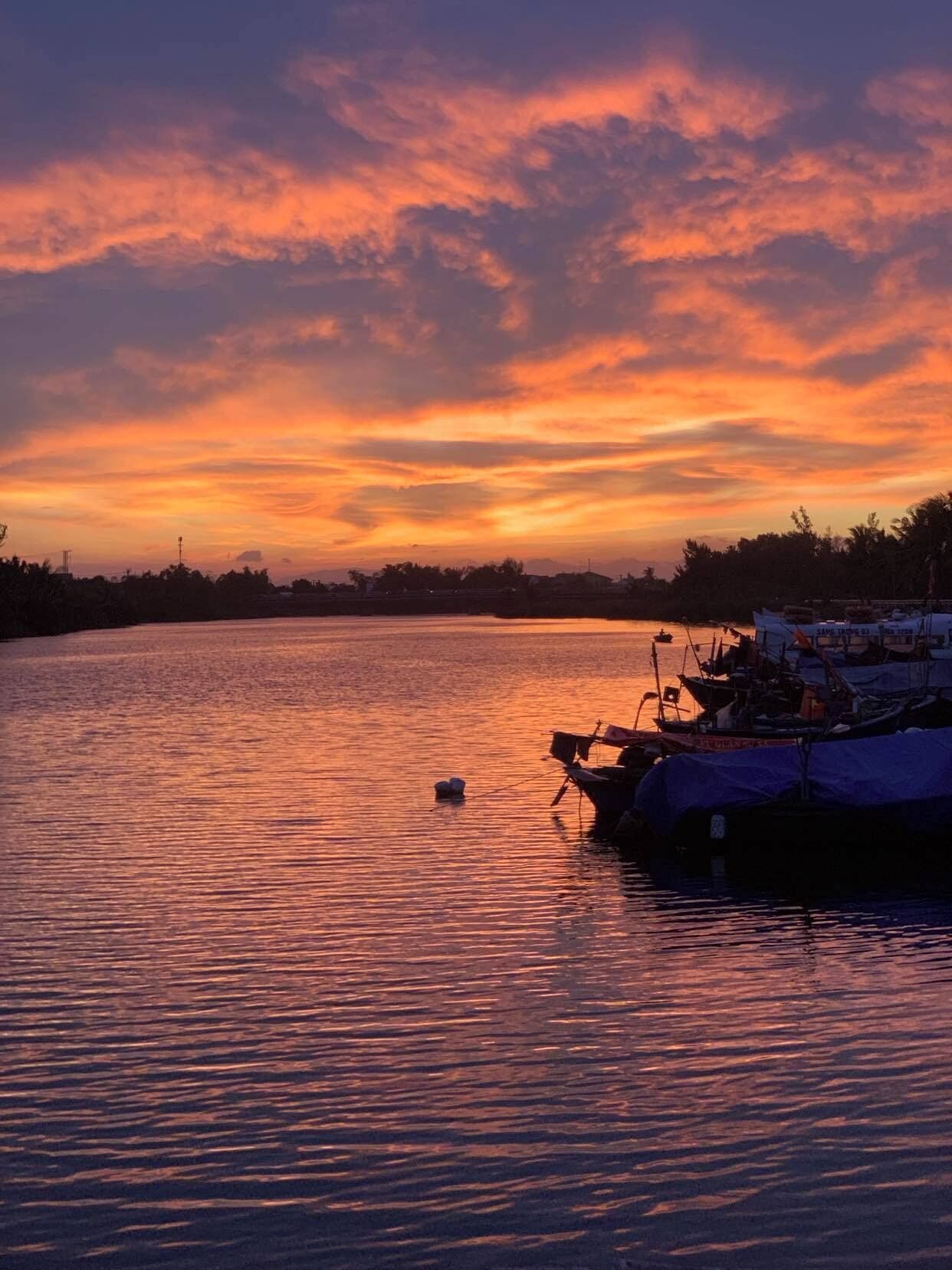 A calm river at sunset with boats docked on the right.