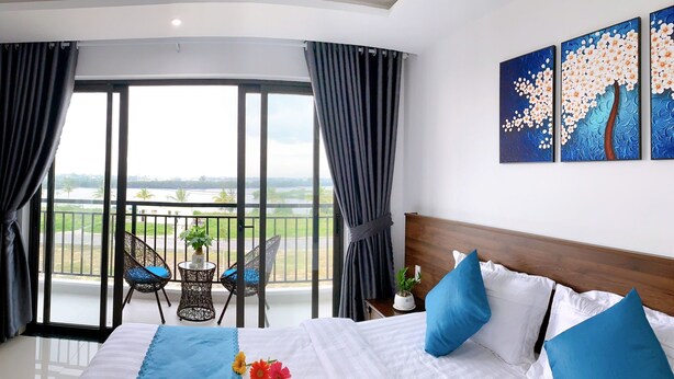 A hotel room with a large bed, a balcony with a view, and a painting on the wall. - EasyLife Villa Hoi An (Da Nang)