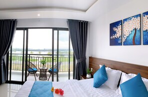 A hotel room with a large bed, a balcony with a view, and a painting on the wall. - EasyLife Villa Hoi An (Da Nang)