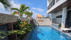 A swimming pool with clear blue water, surrounded by lush greenery and a stone wall. - EasyLife Villa Hoi An (Da Nang)