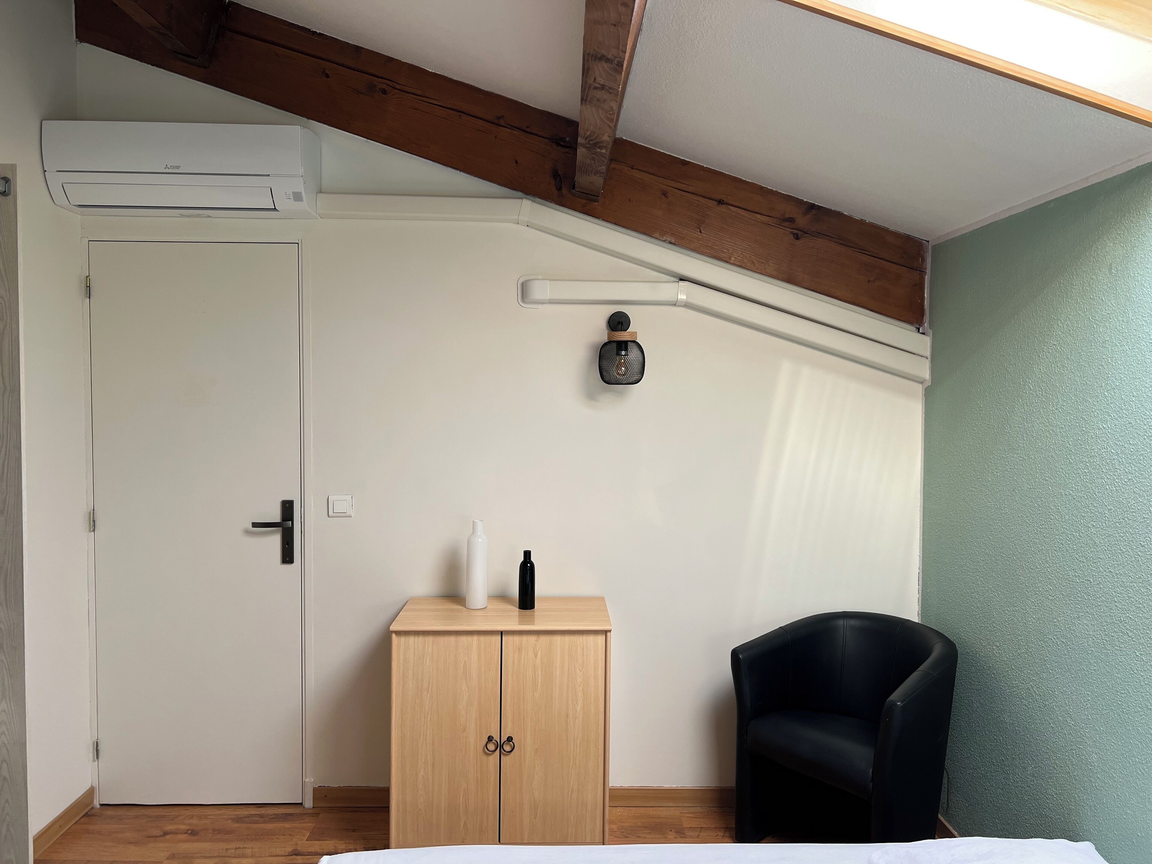 A bedroom with a wooden wardrobe, a black chair, a white door, and an air conditioning unit.