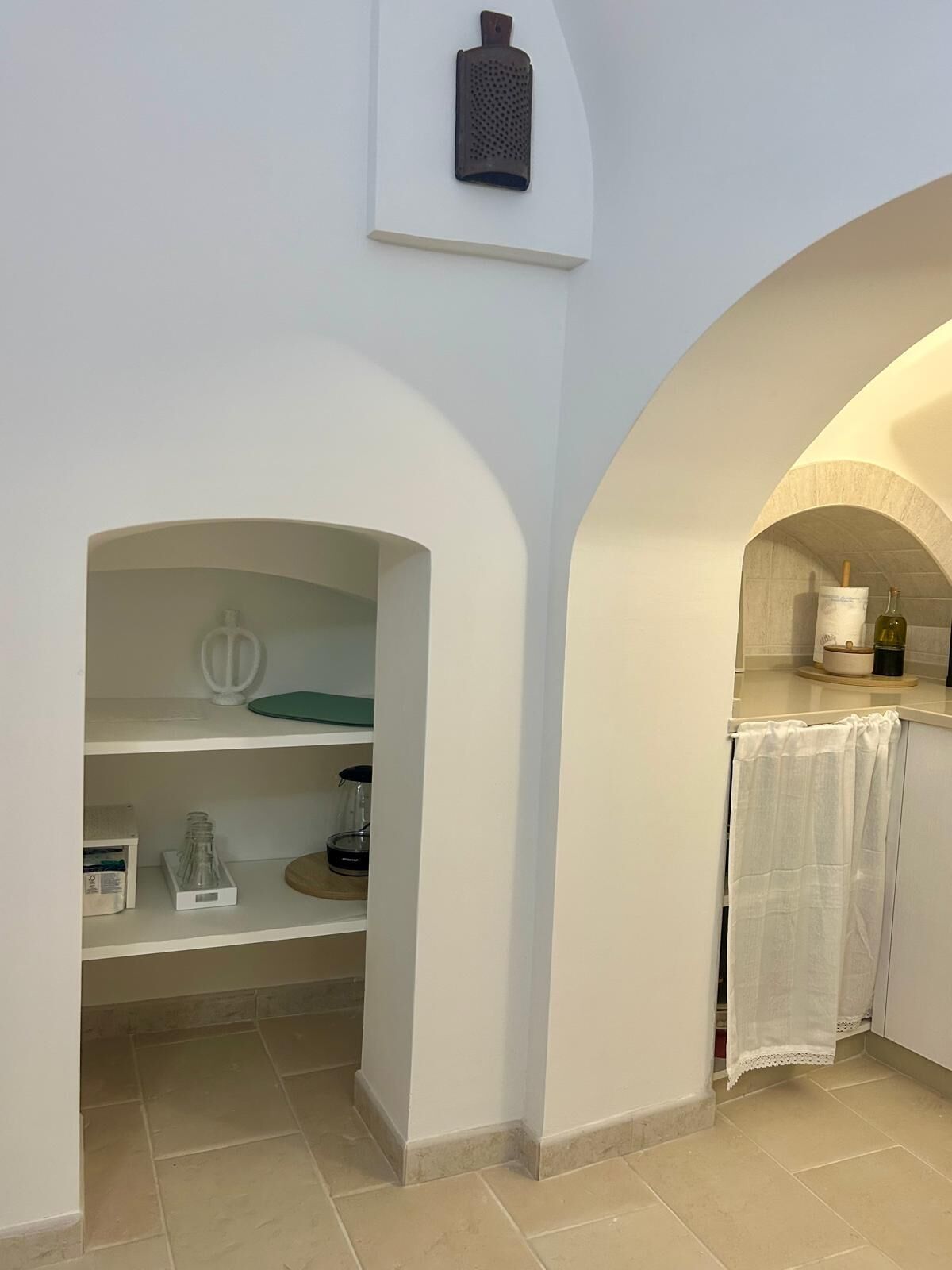A kitchen with white walls, a tiled floor, and a small island with a sink and countertop. There is a wine bottle and a glass on the countertop.