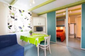 A room with a dining table, chairs, a television, and a bed with a red blanket.