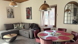 A modern living room with a grey sectional sofa, a round dining table with pink chairs, and artwork on the walls. - L'escapade du cheval blanc, 3 borders, secure parking  (Kembs)