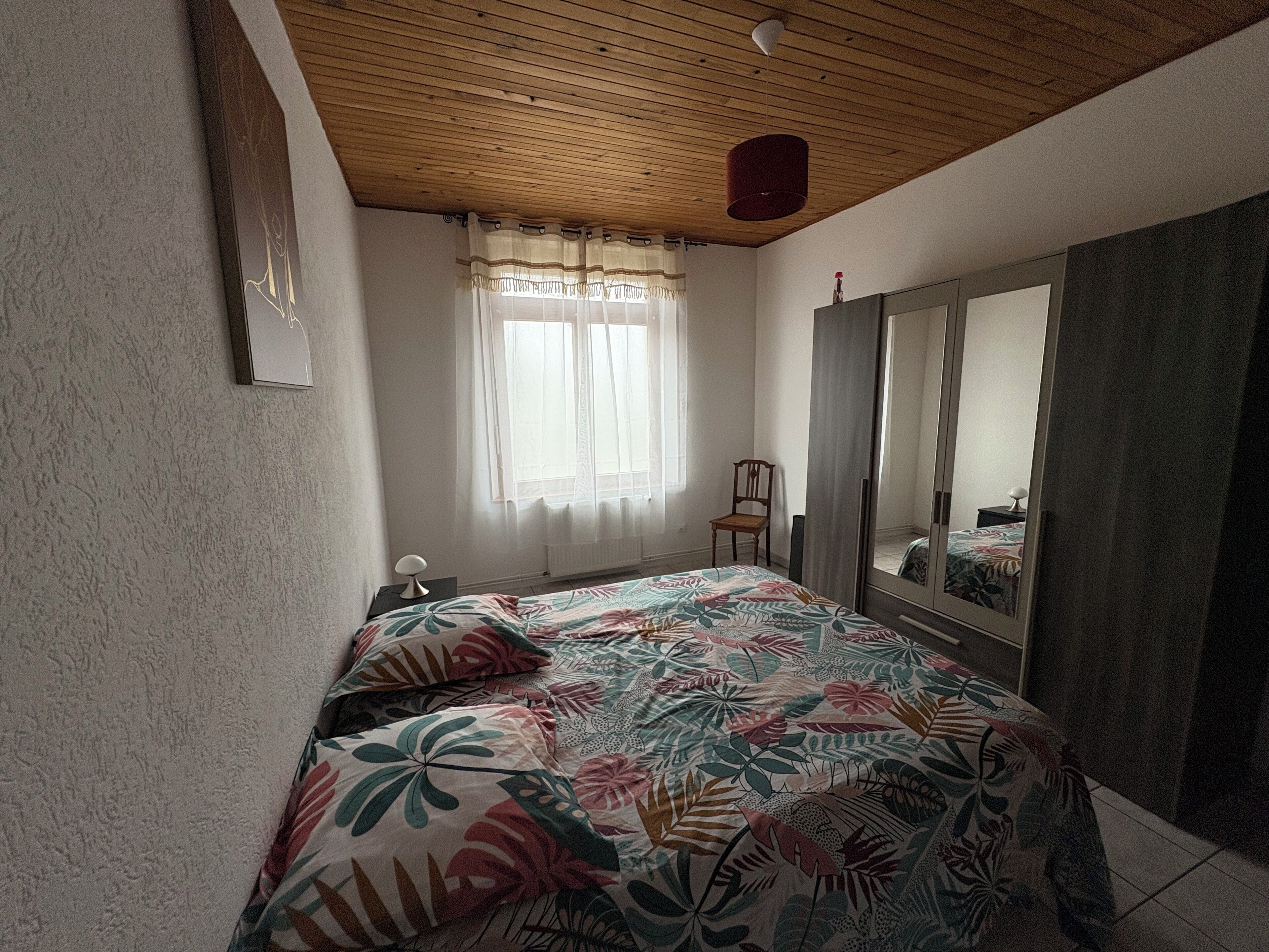 Une chambre à coucher avec un lit, une chaise, une armoire et une fenêtre avec des rideaux.
