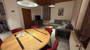 A modern living room with a wooden dining table, red chairs, a grey sofa, and a ceiling light fixture. - L'escapade du cheval blanc, 3 borders, secure parking  (Kembs)