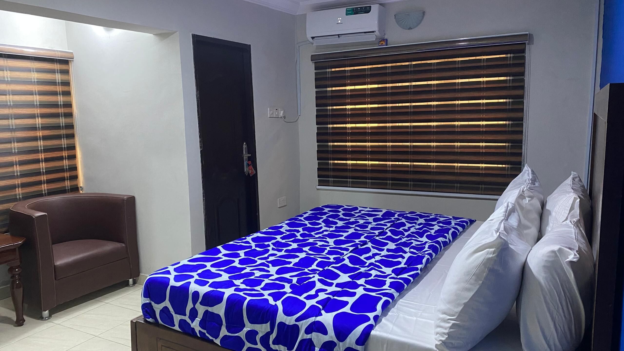 A bedroom with a bed, a chair, a wardrobe, and a window with blinds.