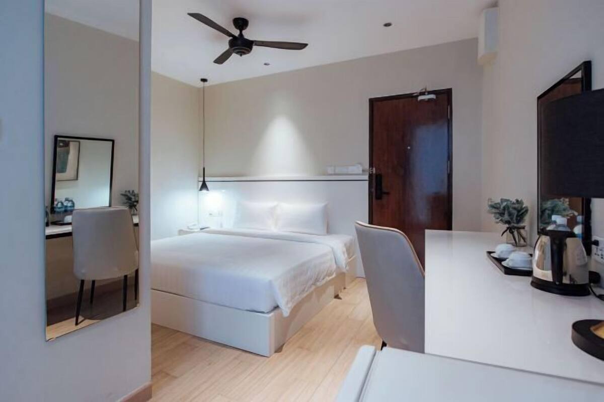 Une chambre d’hôtel avec un lit, un bureau, une chaise, un ventilateur de plafond et une porte.