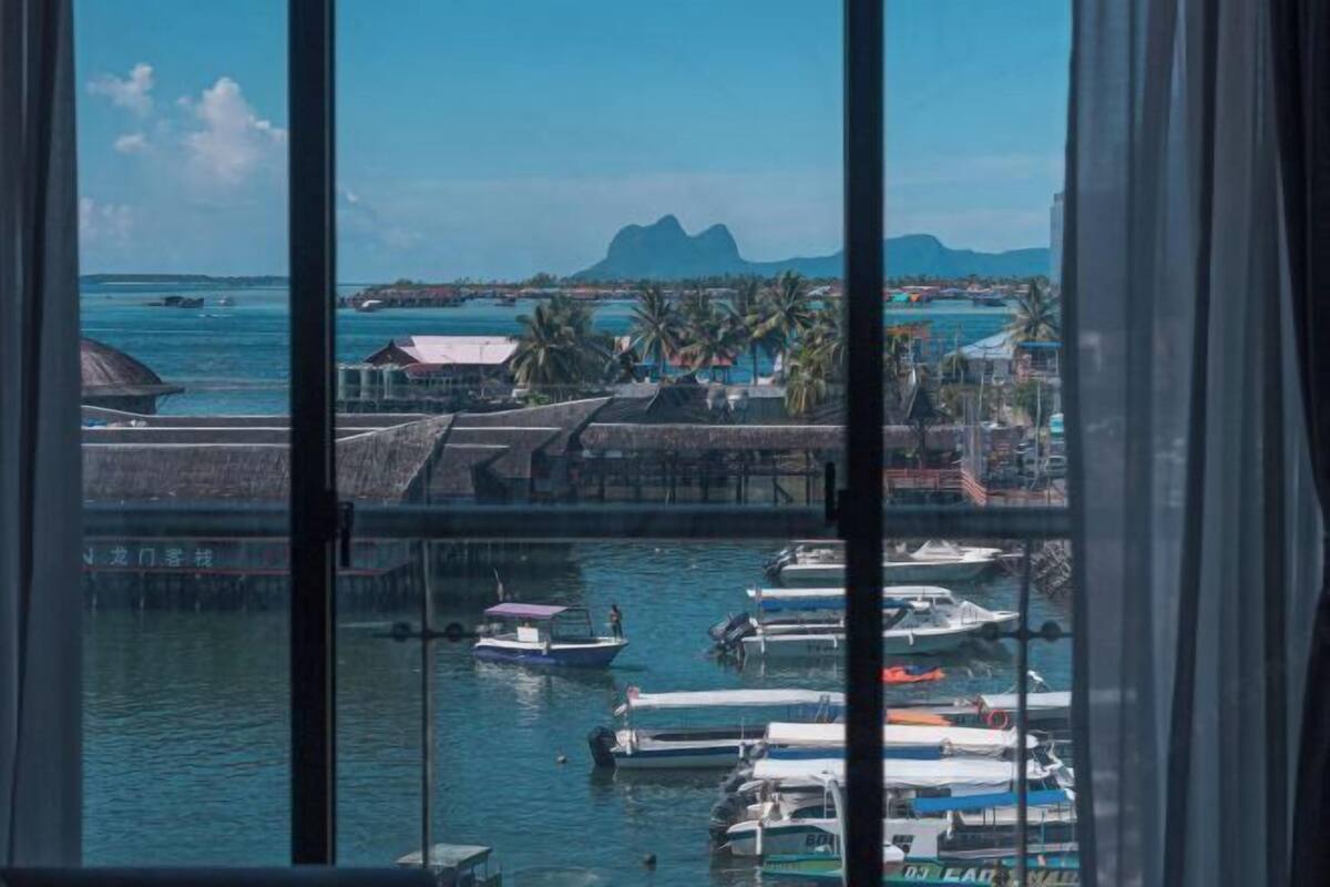 Un port de plaisance avec des bateaux amarrés, une vue dégagée sur la mer et une chaîne de montagnes à l’horizon.
