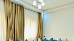 Een moderne woonkamer met een blauwe bank, een houten salontafel en beige gordijnen.