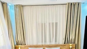 Una cama bien hecha con un cabecero de madera, dos mesitas de noche con lámparas y un amplio ventanal con cortinas.