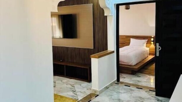 Hotelkamer met een marmeren vloer, een bed met houten hoofdeinde, een aan een houten paneel bevestigde televisie en een plafond met decoratieve details.