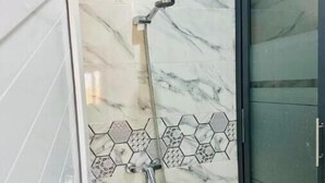 Een badkamer met een douche, marmeren tegels en een glazen deur.