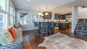 A modern kitchen with a central island, bar stools, and a seating area with a patterned rug.