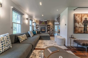 A modern living room with a fireplace, a large sofa, a coffee table, and a painting on the wall.