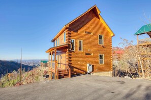A two-story log cabin with a balcony, a covered porch, and a view of the surrounding landscape. - 5-Star Mountain Views • Hot Tub • Blackstone • Game Room • Near Dollywood (Sevierville)