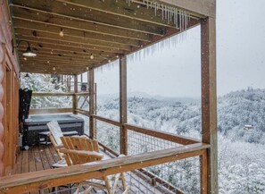 A wooden deck with a hot tub, chairs, and a view of a snowy landscape. - 5-Star Mountain Views • Hot Tub • Blackstone • Game Room • Near Dollywood (Sevierville)