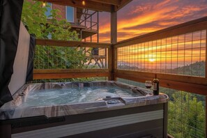 A hot tub with a sunset view, surrounded by wooden railings and a balcony. - 5-Star Mountain Views • Hot Tub • Blackstone • Game Room • Near Dollywood (Sevierville)