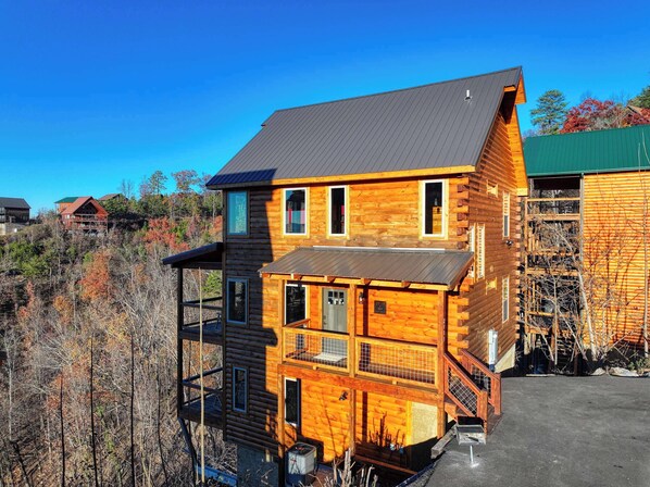 A two-story log cabin with a metal roof, a balcony, and a view of a forested area.