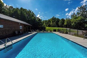 A rectangular swimming pool with a metal ladder on one side, surrounded by a wooden deck and lounge chairs.