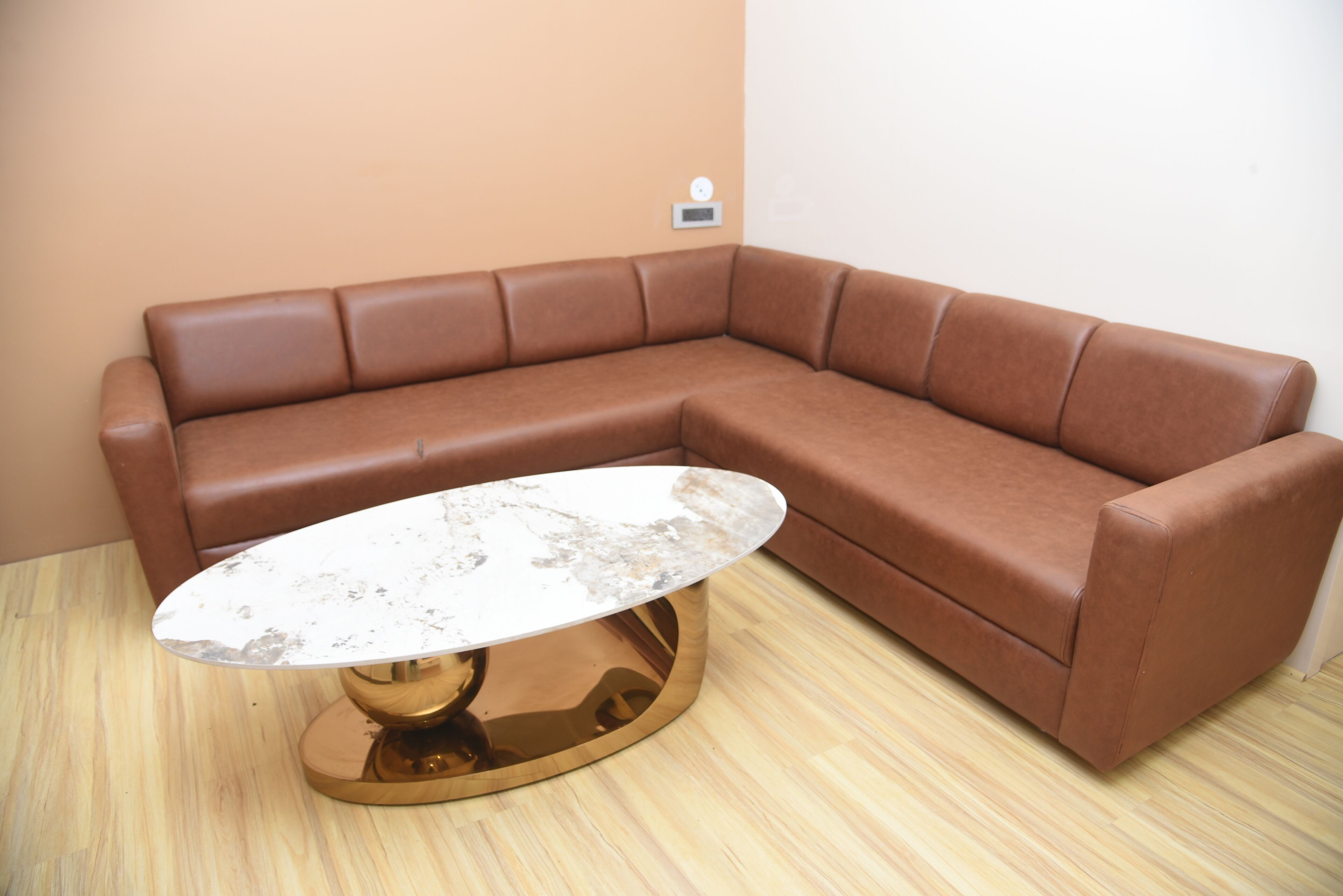 Een bruine leren modulaire bank met een ronde glazen salontafel.