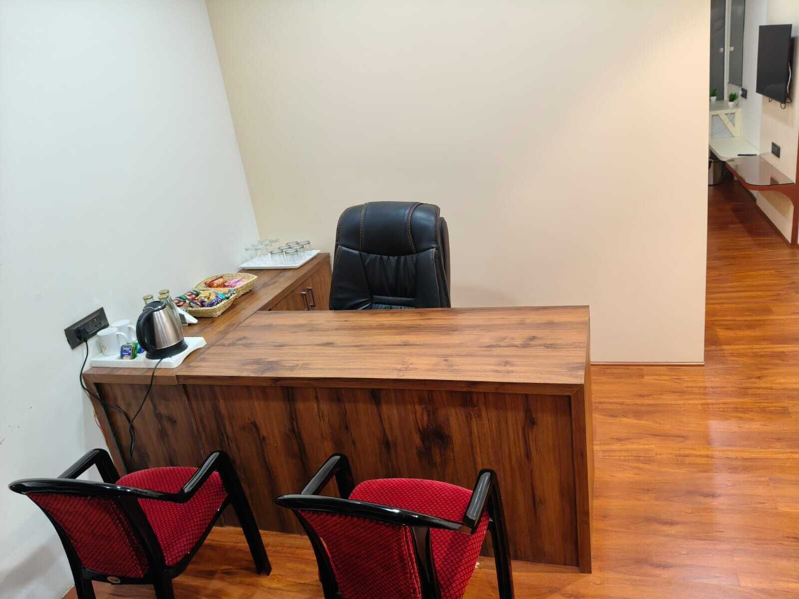 A reception desk with a wooden top, two red chairs, and a black office chair.