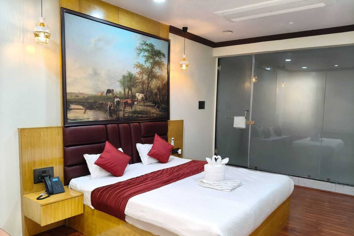 A hotel room with a large bed, a painting, a telephone, and a sliding door.