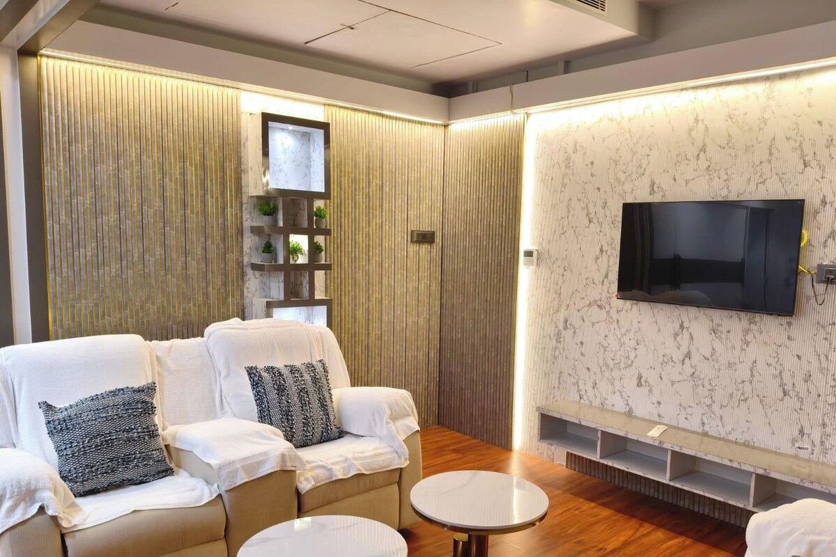 A modern living room with a sofa set, a flat-screen TV, and a built-in shelf unit.