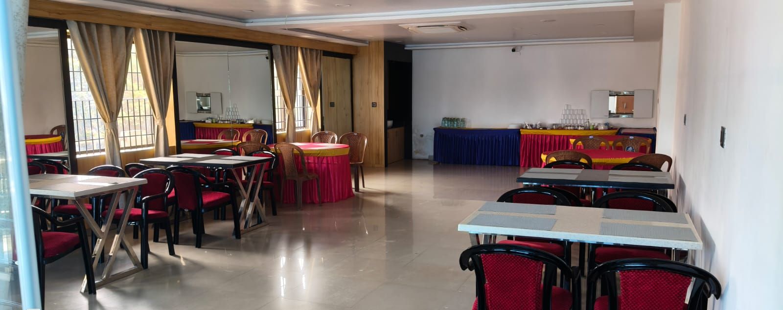 A conference room with tables and chairs, a stage with a blue backdrop, and a kitchen area in the background.
