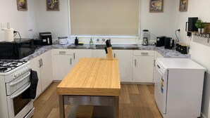 Une cuisine moderne avec des meubles blancs, une table en bois, une cuisinière, un réfrigérateur et une fenêtre avec des stores.