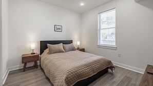 A bedroom with a bed, two bedside tables, a nightstand, a window, and a picture on the wall.