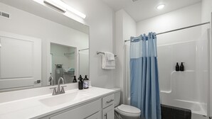 A modern bathroom with a white sink, mirror, and toilet, a shower with blue curtains, and toiletries on the sink.