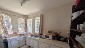 Une cuisine avec des meubles blancs, un four à micro-ondes, un évier et une fenêtre avec des rideaux.