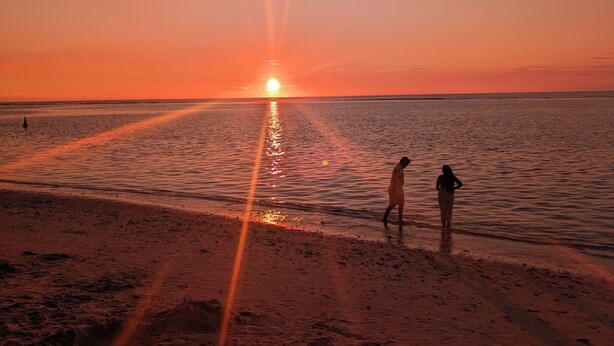 Un coucher de soleil sur une plage, avec deux personnes qui se promènent le long du rivage.